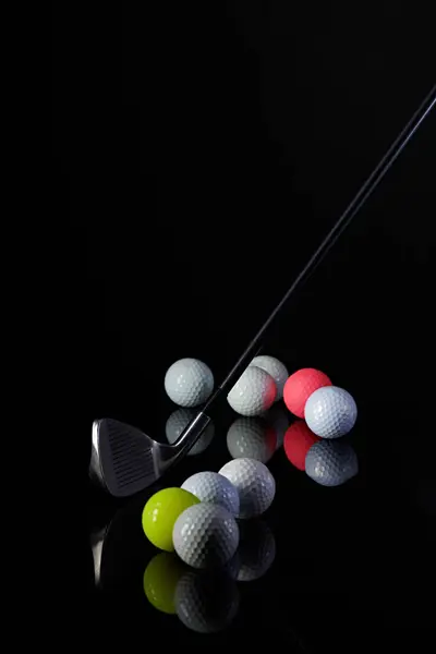 Golf sopası ve golf topu karanlık bir arkaplanda fotoğraflanmış ve fotoğrafta yansımalar var.
