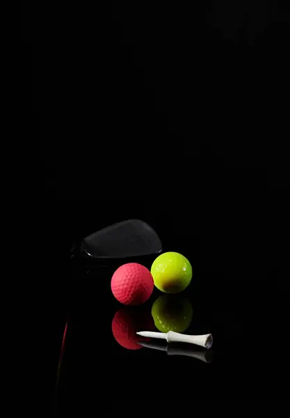 Golf sopası ve golf topu karanlık bir arkaplanda fotoğraflanmış ve fotoğrafta yansımalar var.