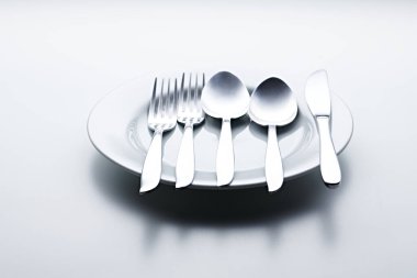 Beyaz arka planda kaşıklar, çatallar, bıçaklar, fincanlar ve plakalar gibi gümüş renkli çatal bıçaklar fotoğraflandı