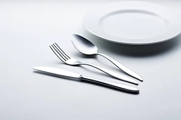 Beyaz arka planda kaşıklar, çatallar, bıçaklar, fincanlar ve plakalar gibi gümüş renkli çatal bıçaklar fotoğraflandı