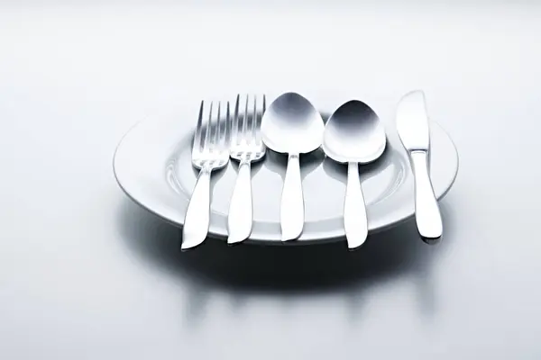 Beyaz arka planda kaşıklar, çatallar, bıçaklar, fincanlar ve plakalar gibi gümüş renkli çatal bıçaklar fotoğraflandı
