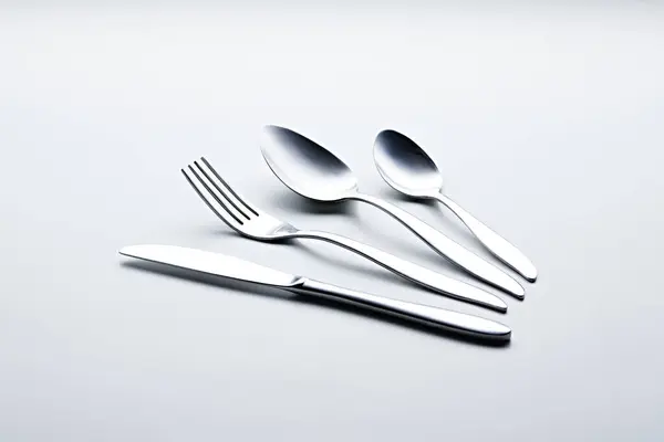 Beyaz arka planda kaşıklar, çatallar, bıçaklar, fincanlar ve plakalar gibi gümüş renkli çatal bıçaklar fotoğraflandı