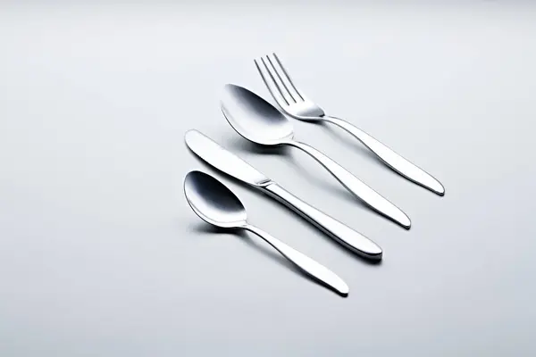 Beyaz arka planda kaşıklar, çatallar, bıçaklar, fincanlar ve plakalar gibi gümüş renkli çatal bıçaklar fotoğraflandı