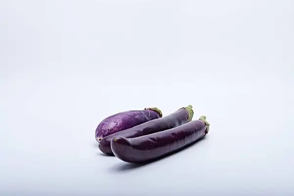 Plastik bir kesme tahtasına yerleştirilmiş taze mor patlıcan beyaz arka planda fotoğraflanmış.