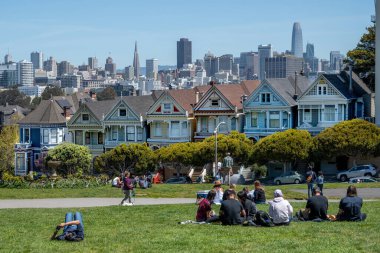 Alamo Square Park, San Francisco, Kaliforniya, ABD - 22 Nisan 2023: Yeşil Park 'ta dinlenen ve bulutsuz mavi gökyüzü altında gün ışığında Boyalı Hanımlar ve Şehre hayran olan mutlu mahalle sakinleri