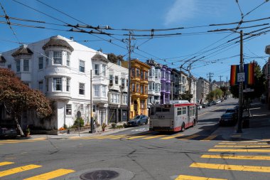 Castro Caddesi, San Francisco, Kaliforniya, ABD - 23 Nisan 2023: Dik sokaktaki renkli evler, asfalt yolda park etmiş arabalar, sarı izler ve bulutlu mavi gökyüzünün altında asılı kablolar