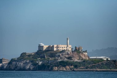 San Francisco, California - 25 Nisan 2023: Alcatraz Adası 'ndaki kayalık sahil şeridinde açık mavi gökyüzüne karşı ünlü müze binası