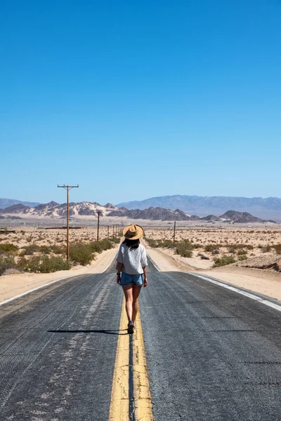 Mojave Çölü, Kaliforniya 'da asfalt bir yolda yürüyen şortlu ve şortlu genç bir kadın.