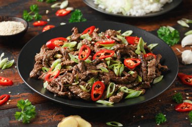 Korean beef Bulgogi with sesame seeds, chili and spring onion in a black plate.