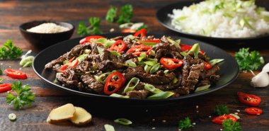 Korean beef Bulgogi with sesame seeds, chili and spring onion in a black plate.