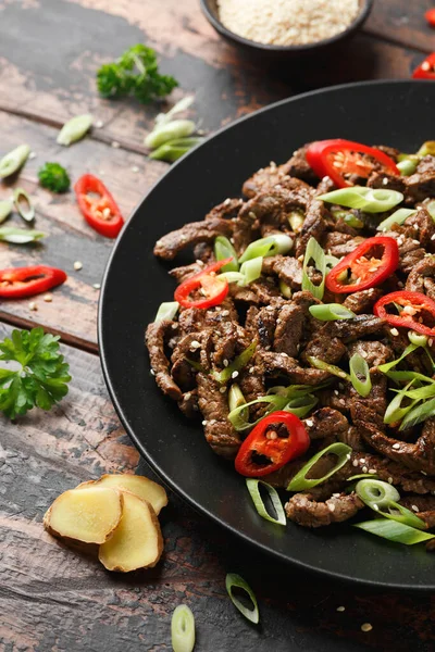 Korean beef Bulgogi with sesame seeds, chili and spring onion in a black plate.