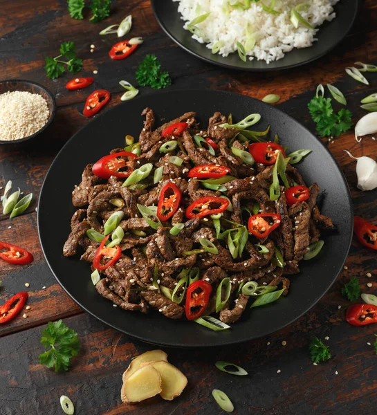 Korean beef Bulgogi with sesame seeds, chili and spring onion in a black plate.