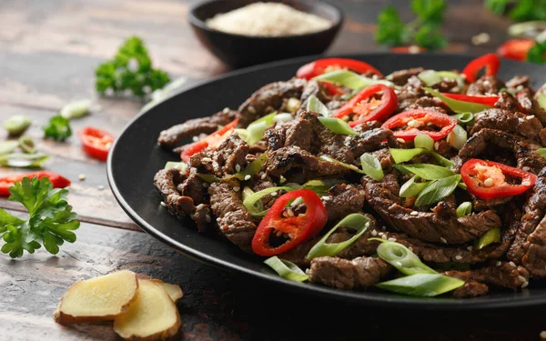 Korean beef Bulgogi with sesame seeds, chili and spring onion in a black plate.