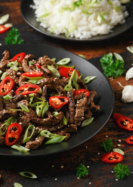 Korean beef Bulgogi with sesame seeds, chili and spring onion in a black plate.