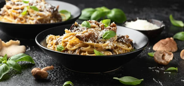 Porcini and woodland mushrooms pasta with pecorino cheese, basil in black bowl.