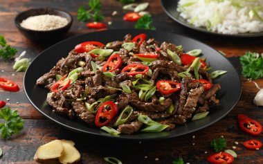 Korean beef Bulgogi with sesame seeds, chili and spring onion in a black plate.