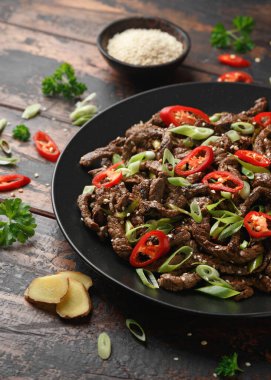 Korean beef Bulgogi with sesame seeds, chili and spring onion in a black plate.