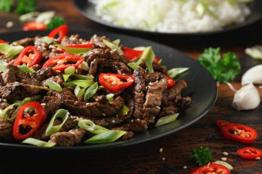 Korean beef Bulgogi with sesame seeds, chili and spring onion in a black plate.