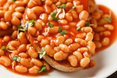Baked beans on toast in tomato sauce on white plate.
