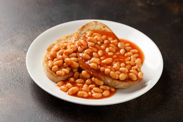 Baked beans on toast in tomato sauce on white plate.