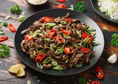 Korean beef Bulgogi with sesame seeds, chili and spring onion in a black plate.