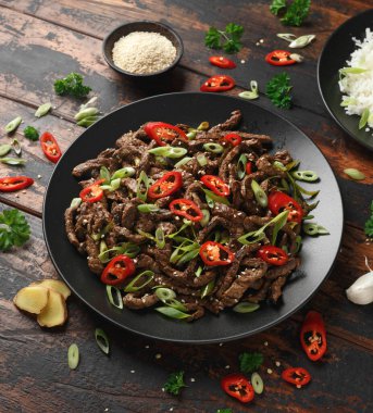 Korean beef Bulgogi with sesame seeds, chili and spring onion in a black plate.