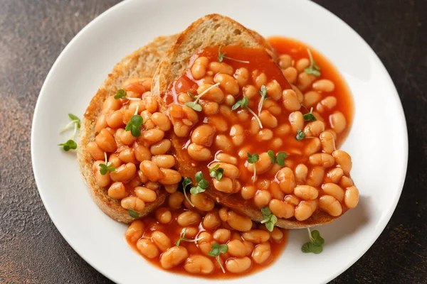 Baked beans on toast in tomato sauce on white plate.