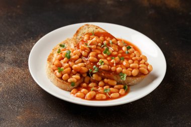 Baked beans on toast in tomato sauce on white plate.