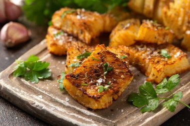 Maydanozlu fırında akordeon patatesi, ahşap tahtada sarımsak ve otlar. Vejetaryen sağlıklı yemek.