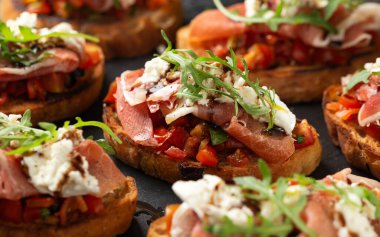 Parma jambonu ve domates bruschetta mozzarella, yaban roketi yaprakları ve balzamik sirkeyle servis edilir..