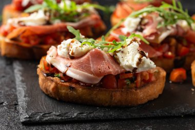 Parma jambonu ve domates bruschetta mozzarella, yaban roketi yaprakları ve balzamik sirkeyle servis edilir..