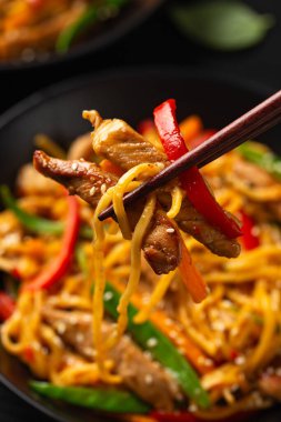 Kızartma chow mein noodle ile siyah kasede domuz eti ve sebze. Asya usulü yemek..