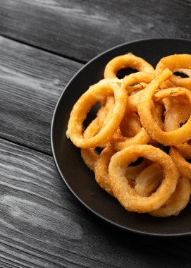 Çıtır çıtır kızarmış soğan halkaları siyah tabakta..