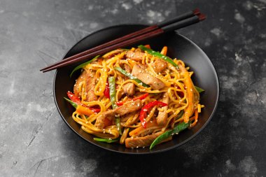 Kızartma chow mein noodle ile siyah kasede domuz eti ve sebze. Asya usulü yemek..