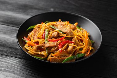 Kızartma chow mein noodle ile siyah kasede domuz eti ve sebze. Asya usulü yemek..