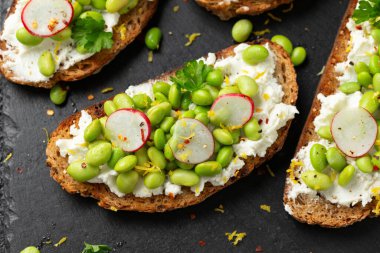 Soya fasulyesi ve keçi peyniri, ekşi ekmek bruschetta limon lezzeti ve kırmızımsı siyah tahtada servis edilir..