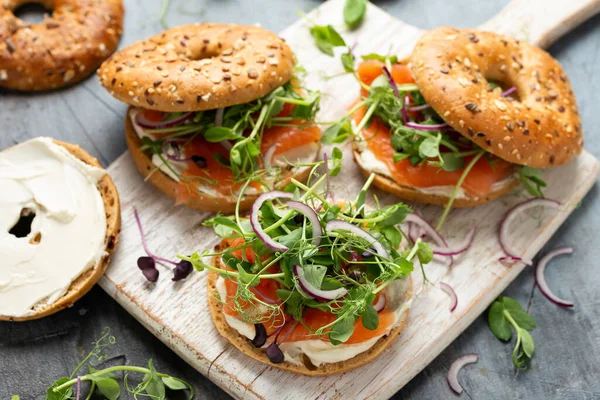 Smoked salmon and soft cheese seeded bagel with pea and purple reddish shoot salad and red onion. Protein packed breakfast concept.