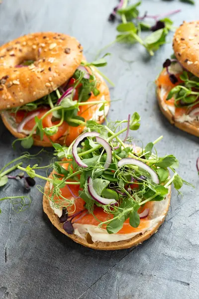 Smoked salmon and soft cheese seeded bagel with pea and purple reddish shoot salad and red onion. Protein packed breakfast concept.