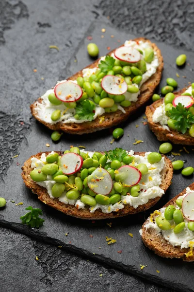 Soya fasulyesi ve keçi peyniri, ekşi ekmek bruschetta limon lezzeti ve kırmızımsı siyah tahtada servis edilir..