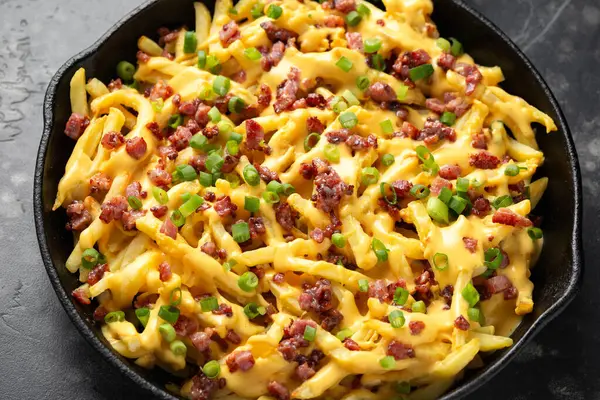 Crispy French fries loaded with bacon, cheese sauce and spring onion in iron cast pan.