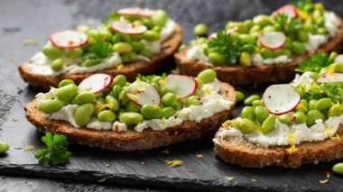 Soya fasulyesi ve keçi peyniri, ekşi ekmek bruschetta limon lezzeti ve kırmızımsı siyah tahtada servis edilir..