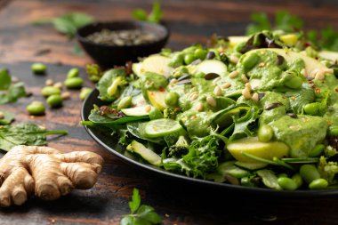 Ispanak, brokoli, elma, salatalık ve edamame fasulyeli süper yeşil salata avokado, elma sirkesi ve zeytinyağı sosu, çam fıstığı ve balkabağı çekirdeği ile servis edilir..