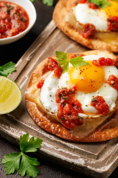 Huevos Rancheros tostadas omlet, domates salsası, fasulye ezmesi ve peynir tahtada..