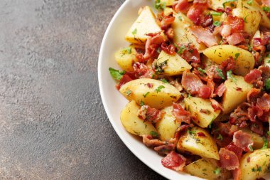 Beyaz tabakta domuz pastırması ve otlu Alman Patates Salatası..