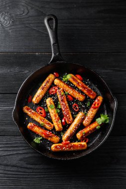 Yapışkan Teriyaki sosisleri susam tohumları, acı biber ve dökme demir bir tavada otlar..