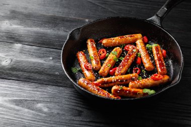 Yapışkan Teriyaki sosisleri susam tohumları, acı biber ve dökme demir bir tavada otlar..