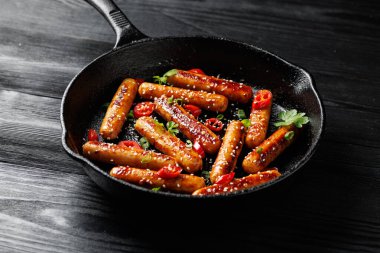 Yapışkan Teriyaki sosisleri susam tohumları, acı biber ve dökme demir bir tavada otlar..