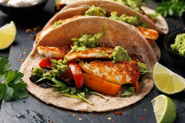Kavrulmuş soğan ve dolmalık biber, avokado guacamole ve biber turşusu ile kızarmış halloumi fajitas..