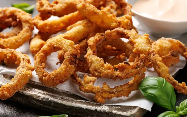 Ahşap tahtada soslu kızarmış soğan halkaları..