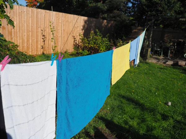 A washing line with colourful pegs and different colour towels hanging to dry in the sun